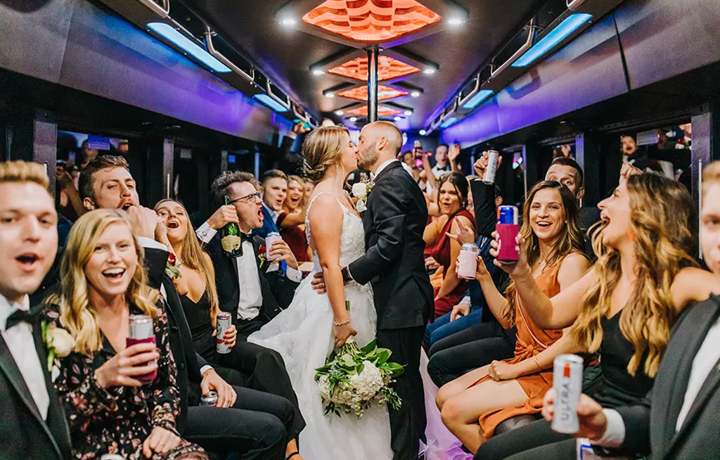 A bunch of people seeing the couple kissing on the wedding party bus
