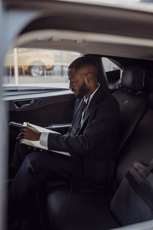 A man in business attire reviewing paperwork in the back of a luxury car.